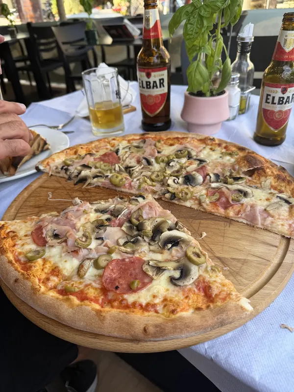 Two pizzas on wooden boards with bottles of Elbar beer on a terrace table