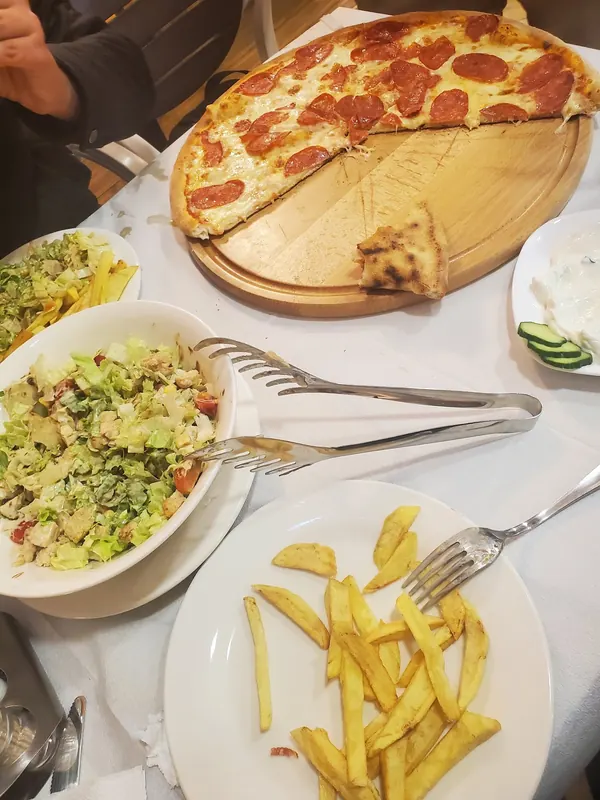 Salads, fries and a salami pizza shared on one table