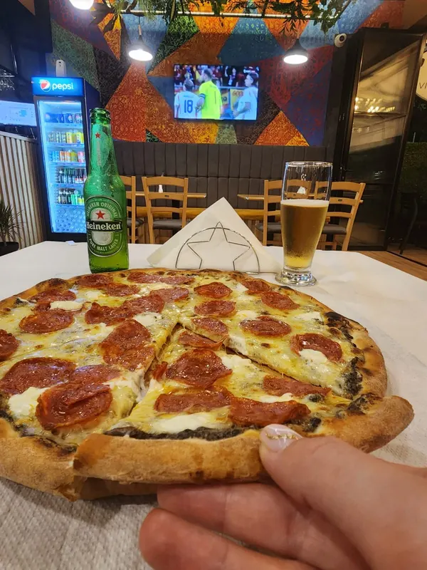 Salami pizza on a white tablecloth with a Heineken and a glass of beer