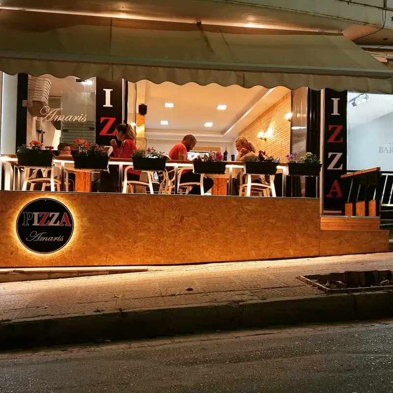 An evening view of a Pizza Amaris front with a round lit sign